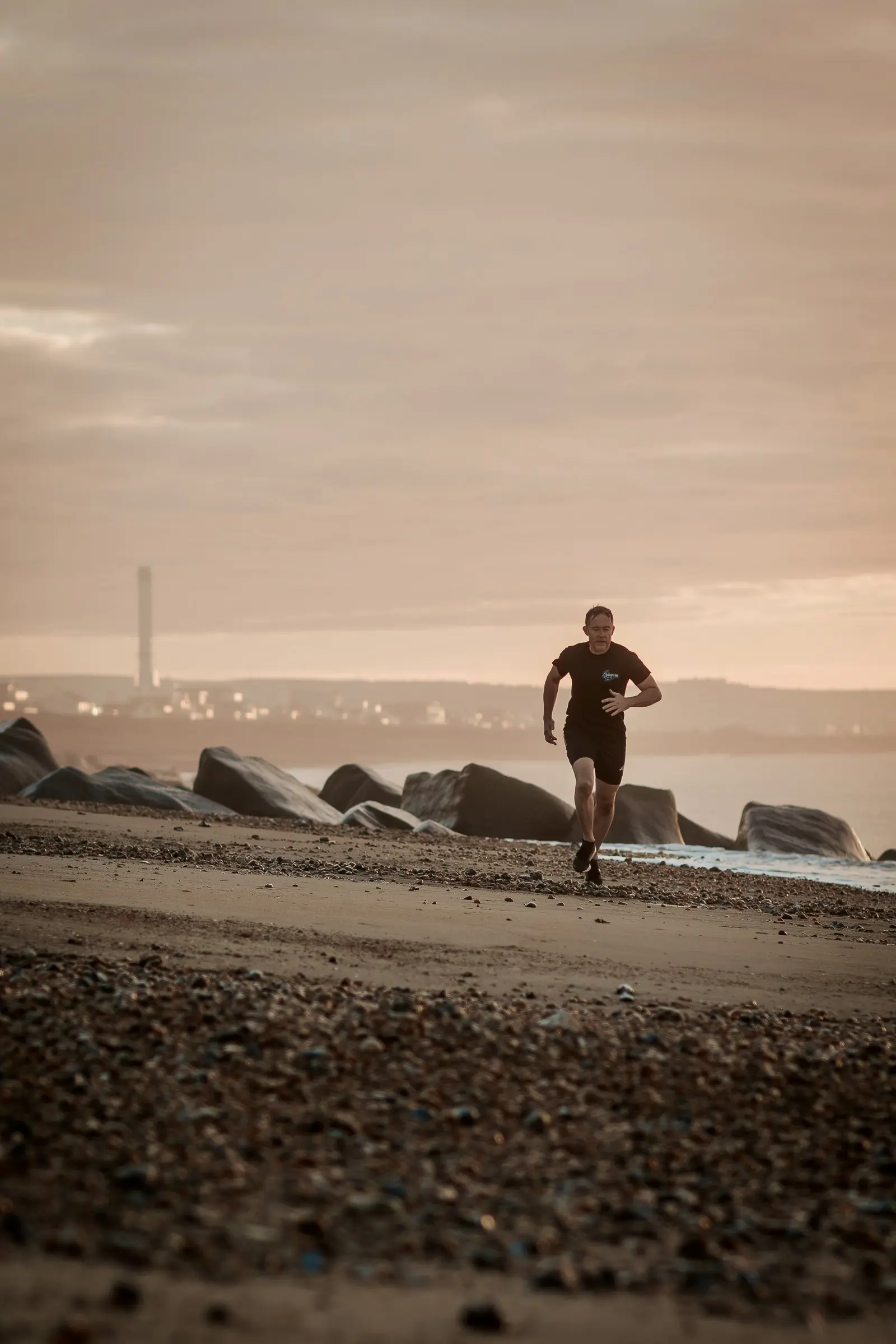 Mark running along the shingle towards the camera at sunrise, the power station chimney behind