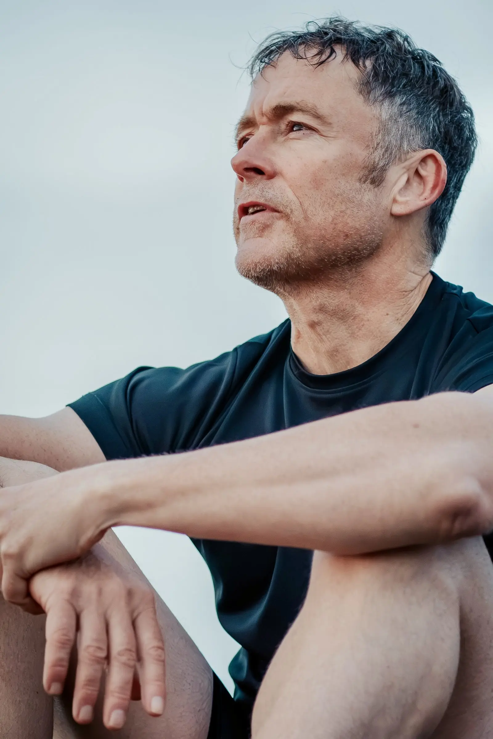 Close-up of Mark sitting with his arms folded on his knees, looking out to sea