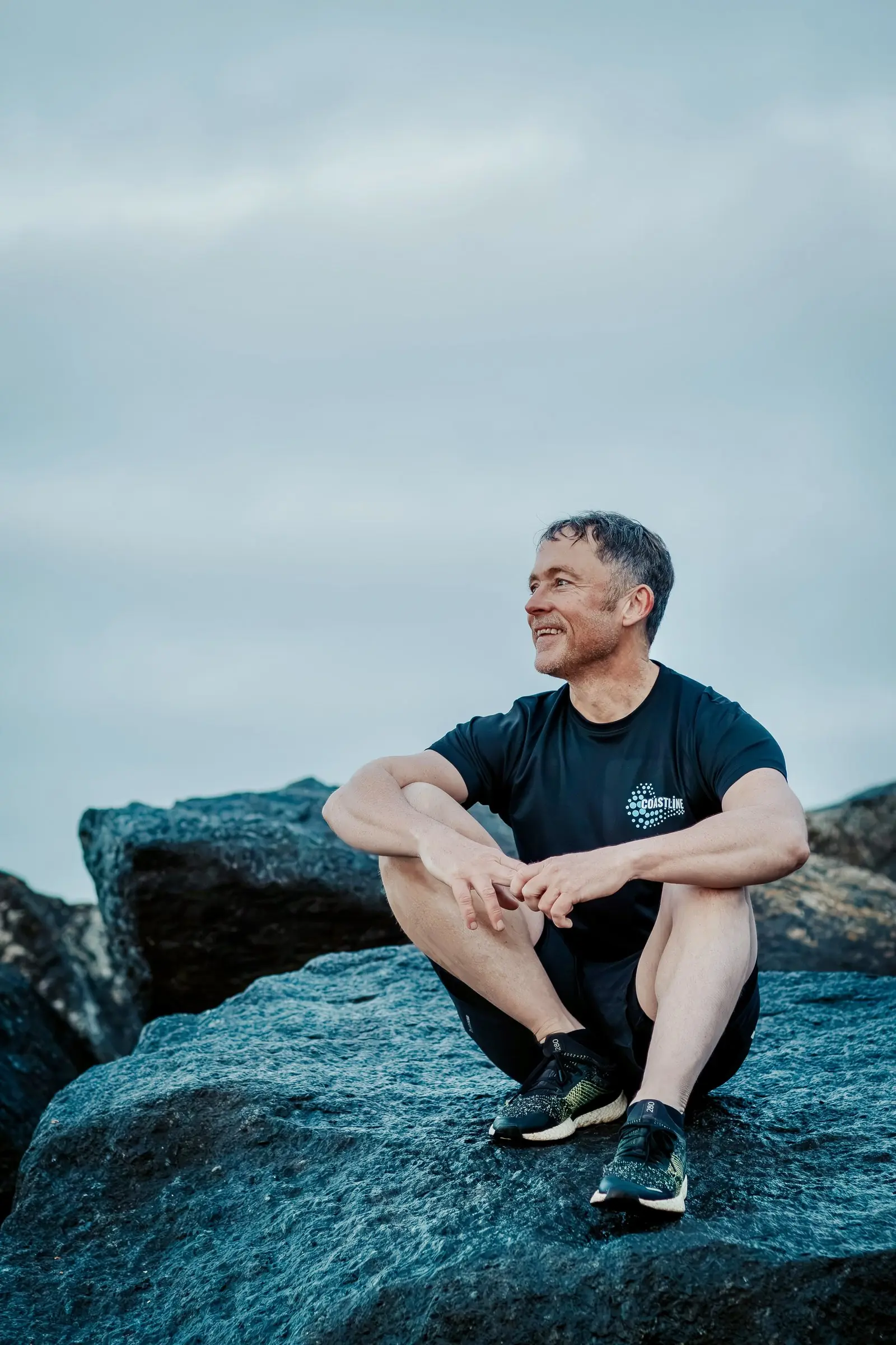 Mark sitting on a rock, looking off to one side and smiling