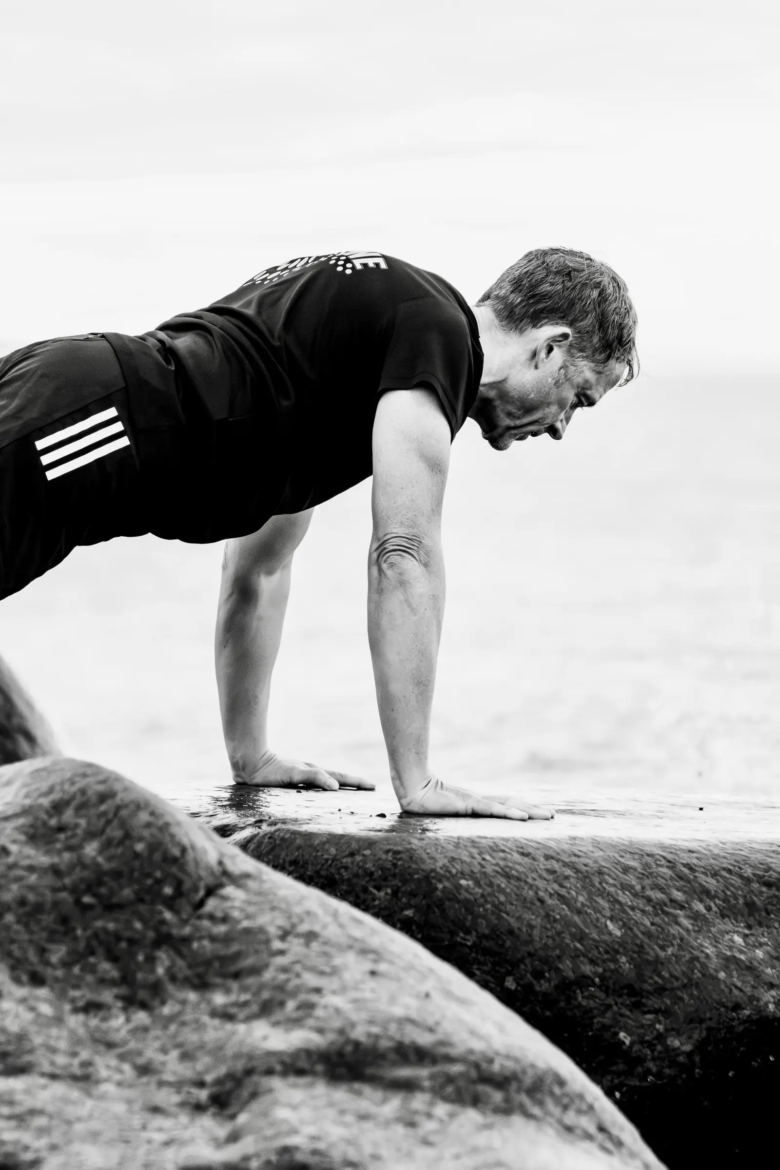 Black and white photo of Mark doing a press-up on a smooth rock