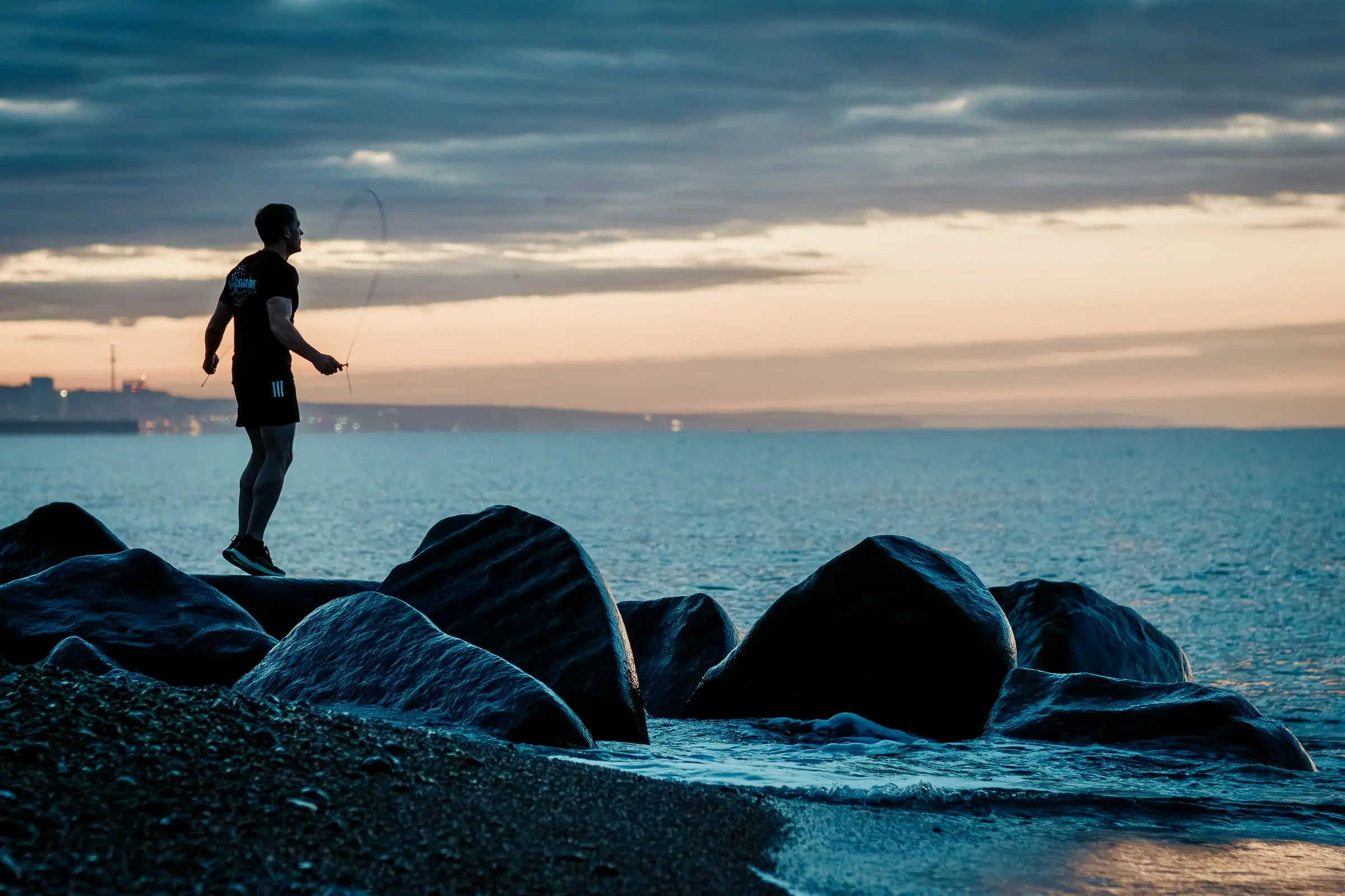 Mark skipping with a rope on a rock groyne at dawn, the sea calm behind him