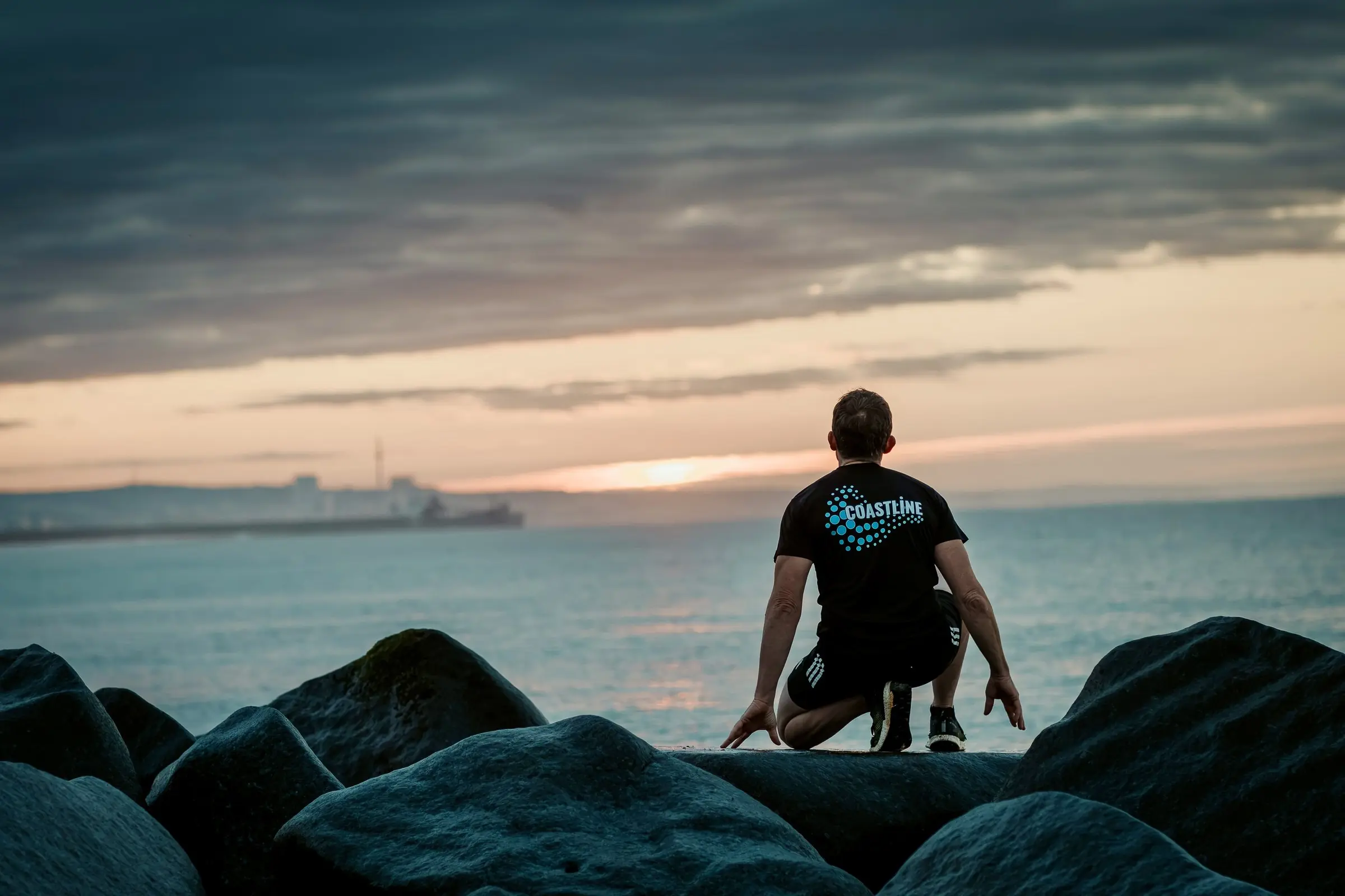 Mark kneeling on a rock groyne on Shoreham beach, watching the sun rise over the sea